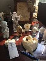 Photo showing multiple religious-themed figurines on a table including crystal angel, praying babies, oval plaque, baby in shell, and framed Lord's Prayer.
