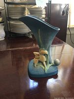 Front angled view of the blue-green Roseville cornucopia vase showing the floral Zephyr Lily design with raised lilies and leaves.