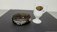 Lot contents showing both the white glass 1972 Grey Cup coffee cup and the black glass ashtray with white lettering on the side.