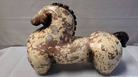 Side view of ceramic horse sculpture showing rounded body, distinctive mane and tail, mottled paint finish.