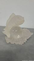 Front view of frosted glass fish sculpture holding a clear glass ball, showing textured fish details and the glass ball in the center.