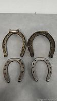 Four metal horseshoes arranged on flat surface: two larger ones on top and two smaller below, showing varied metal textures and wear.