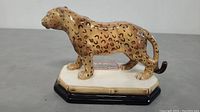 Side view of the ceramic leopard figurine on its base showing the detailed spots and shape.