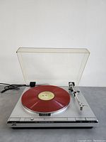 Front angle showing turntable deck, tonearm, red vinyl record, and open dust cover