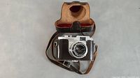 Front view of camera inside brown leather case with strap, showing overall condition.