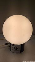 Side view of the vintage white glass globe table lamp showing the lit globe and black base with on/off switch and lot sticker.