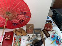 Overview of the lot showing parasols, wooden sandals, hand painted fans, carved wood box, lacquer tray, vintage doll, silk wallet with yen notes and decorative items on white bedding