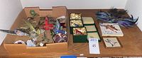 Wide view showing the assortment of bird and butterfly ornaments including many small bird figures, butterfly ornaments, and a couple of glass paperweights, spread in a cardboard box and on the surface around it.