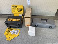 Four tool kits in original boxes and cases arranged on ground: DeWalt sander kit with box and case, cardboard box for scroller saw, Dremel carrying case, and Dremel router attachment box.