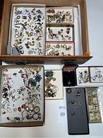 Multiple small trays showing a wide variety of earrings, rings and a pendant spread across a wooden drawer