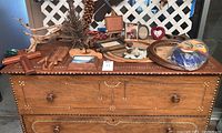 Front view of four-drawer wood dresser with white decorative inlay and assorted decor on top including picture frames, wooden items, and a paper mask.