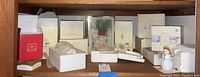 Shelf with multiple boxed Lenox items including vases, plates, mugs, and figurines plus a snowman figure outside box.