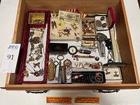 Drawer contents showing assortment of men's vintage accessories including cufflinks, old keys, pocket knives, watch fob, and other small collectibles spread across compartments.