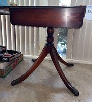 Side view of square mahogany table with drop leaf extended, central pedestal, and curved legs ending in claw feet.