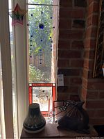 Photo of the pottery, stained glass, reindeer statue and temperature gauge arranged on a brick ledge by window with sunlight.
