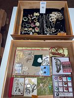 Wide top view of two drawers containing assorted jewelry: rhinestone brooches, pearl-type necklaces, earrings, pendants, and hat pin.