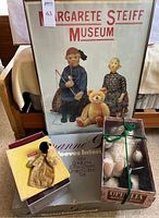Overview of lot: framed Steiff museum poster leaning, Goldilocks & The Three Bears box, Ophelia/panda box tied with green rope and small dog puppet box