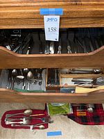 Drawer open showing multiple silverware pieces including forks and spoons of various styles and patterns, some in cloth rolls.
