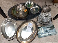 Overview photo showing various silver plated trays, bowls, and serving pieces spread on the floor with lot stickers.
