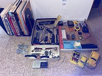Display of the assorted small hand tools, wristwatches, pocket knives, model cars, mini tape recorder, and camping silverware arranged on the floor.
