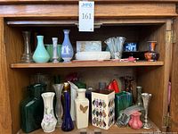 Full shelf view showing assortment of vases in various materials, colors, and sizes on wooden shelf.