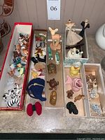 Full view of all ceramic animal figurines arranged in four narrow trays showing a variety of small vintage animals including zebras, birds, turtles, a deer, and two wedding figurines of bride and groom.