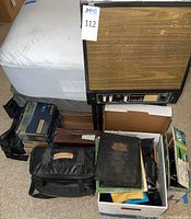 Photo showing assorted camera bags, projector, boxes and cases on floor and mattress.