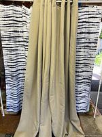 Two curtained panels hanging, oat color with silver grommets visible on the top, panels placed in front of black and white curtains.