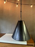 Front view of large conical metal ceiling lamp shade in matte black finish.