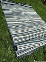 Indoor outdoor rug unrolled on grass showing striped design and flat woven texture.