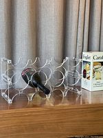 Two clear lucite wine racks with rounded spaces for holding bottles horizontally. One rack shown with a bottle inside, the other empty. A Danish Holmegaard carafe in box seen beside them.