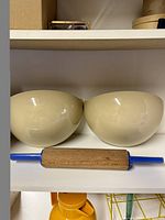 Photo showing two beige half moon wall planters and blue melamine handled wooden rolling pin on a shelf.