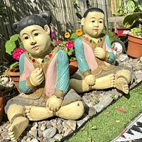 Pair of mid century hand carved wooden figurines seated cross-legged with colorful painted details and gilt accents.