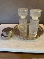 Full view of the lot including two clear textured glass decanters with screw tops, a silver plated gallery tray, and two silver plated trinket boxes stacked.