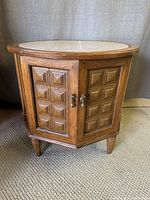 Front view of a mid-century wooden cabinet with a round travertine top, single door featuring square panel design, and metal handles.