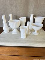 Front view of all nine milk glass pieces on display, showing diverse shapes and textures.