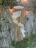 Full view of onyx angel fish wind chime hanging outdoors with bamboo fence background, sun shining from top right.