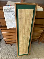 Wooden rectangular Shuffleshot tabletop game board with scoring lines, green felt padding around the board, and a surrounding wood frame next to a folded instruction sheet.