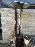 Full view of the propane patio heater lamp showing the rust-colored base, vertical body, and top metal canopy with slight dents.