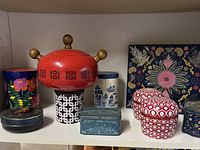 Eight assorted tins displayed on a shelf showing various colors and shapes including floral and geometric designs.
