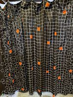 Large black curtain panels with white grid and orange square pattern, gathered on a curtain rod.