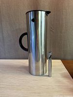 Full view of the Stelton Thermo jug with black handle and a metal bottle opener placed in front