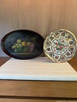 Two trays displayed together, showing the oval fruit basket tray and round floral tin tray