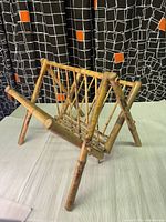 Front and side angled view of the vintage burnt bamboo boho chinoiserie magazine rack, showing frame and crossed bamboo slats with burn marks in lacquered finish.