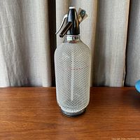 Front view of vintage Czech seltzer bottle covered in white metal mesh showing entire bottle and dispensing head.