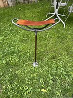 Vintage Featherwate shooting stick standing on grass with metal frame and brown leather seat