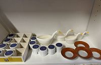 12 vintage Ikea PS Varmeljushallare ceramic candle holders including tea lights displayed with swan measuring cups and orange gold tea light dishes.