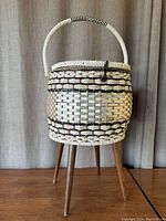 Front view of vintage wicker sewing basket with wrapped handle and wood hairpin legs