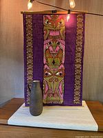 Full view of the brutalist vase in front of owl motif wall hanging