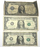 Front of three $1 American bank notes including one Silver Certificate and two Federal Reserve Notes.